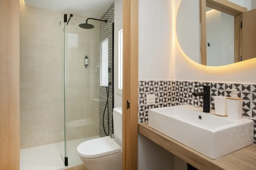 Casa Vacacional Baño moderno con azulejos geométricos, espejo redondo iluminado y ducha de cristal
