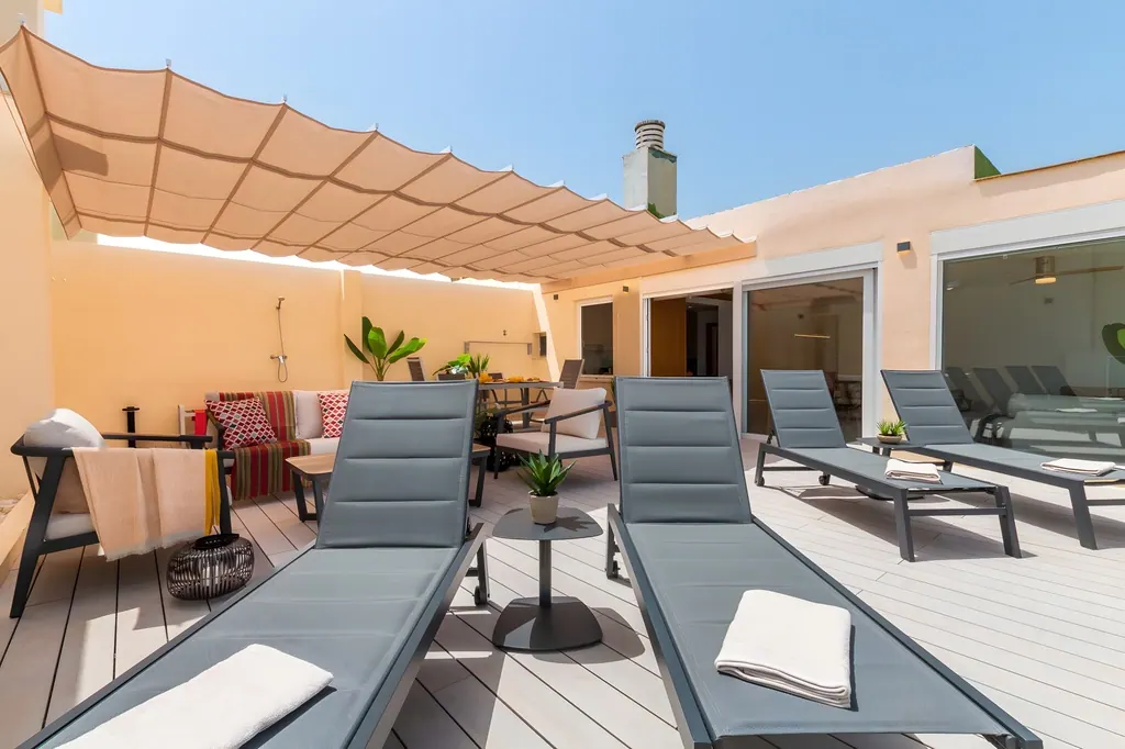 Ático en la Carihuela Terraza moderna con tumbonas grises y toldo beige en ático