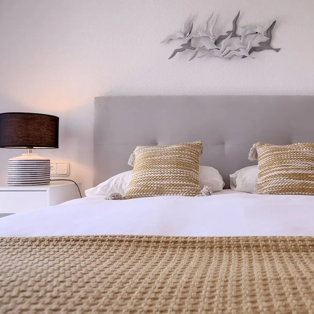 Las Gaviotas Dormitorio moderno con cabecero gris, cojines beige y lámpara decorativa